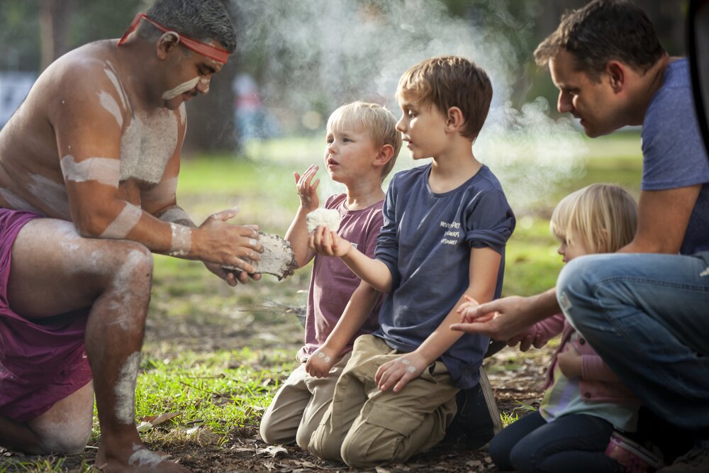 Aborigine mit Kindern beim Feuer machen
